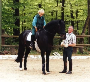 Rider on black horse and trainer standing beside them